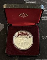 Canadian silver proof dollar coin in black presentation case with red velvet interior and silver maple leaf emblem on lid.