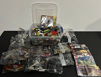 Overview of LEGO lot with clear plastic bin full of loose bricks, multiple numbered sealed bags of LEGO pieces, and various LEGO instruction manuals. Boxed LEGO Creator 3-in-1 set visible.