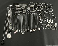 Full lot view showing all silver tone jewelry items laid out on black surface, including necklaces, bracelets, hoop earrings, stud earrings, and rings.
