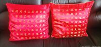 Two red silk pillows featuring gold Chinese characters arranged in rows, measuring approximately 40cm by 40cm each.