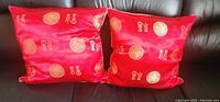 Two red silk pillows with gold printed 福 characters and circular designs shown on a dark sofa.