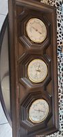Wooden barometer, thermometer, and hygrometer set in dark wood frame with brass-rimmed dials.