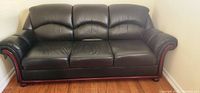 Front view of a black leather sofa with wooden base and armrests, placed on hardwood floor