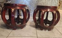 Two small round rosewood stools with open vertical slats and inlaid floral designs on top edges and surfaces, showing minor damage on top.