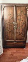 Front of wooden armoire showing hand-painted tree branch and leaves design on the doors, door handles, and lower drawers