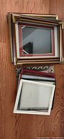 Photo showing a stack of eight assorted picture frames including gold-toned metal, wood, and plastic frames of various sizes and colors.