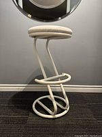 Side view of one white tubular metal frame 1970s mid century modernist French bar stool with beige round seat cushion.