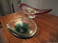 Two mid century modern glass art console bowls displayed on a wood surface: pink signed Chalet bowl and green unsigned bowl.