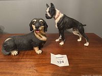 Photo showing both dog figurines, Bull Dog and Dachshund, on a wood surface with lot tag 124 visible.
