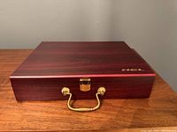 Closed dark wood box with gold handle and latch, engraved HCL logo on top right corner