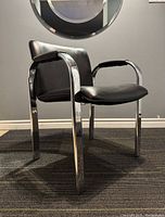 Side angle view of the postmodern armchair showing the chrome frame, black upholstered seat, and padded armrest.