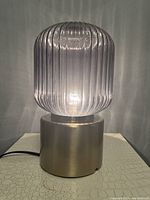 Table lamp illuminated showing ribbed gray clear glass shade and brass base.