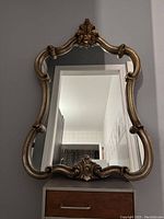 Full view of the vintage French Rococo style mirror showing its ornate gold-toned frame and reflective surface.