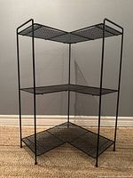 Front angled view of vintage meshed metal corner stand showing three levels with mesh shelving and tubular metal frame.