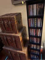 Tall black CD rack filled with CDs and three vintage-style leather boxes stacked beside it.