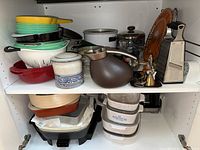 Shelves with assorted cookware including colorful pots, bowls, a kettle, and kitchen tools