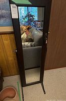 Full view of closed dark wood framed floor mirror on stand