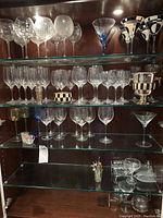 Shelf with etched and plain wine glasses along with black and white patterned and blue-stemmed martini glasses.