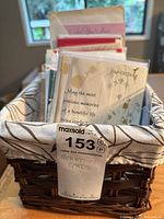Collection of greeting cards arranged standing in a decorative fabric-lined woven basket, includes various cards with visible text and envelopes.