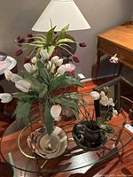 Photo showing the table lamp with spiral shell base and beige shade, along with several faux flower arrangements and decorative vases on glass table