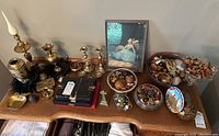 Wide shot of all lot items arranged on wooden surface, including brass decor, bowls with potpourri, framed print, and silverware case