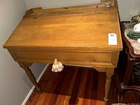 View of the front and top panel of wooden secretary desk with tassel on keyhole, showing desk's condition and style.