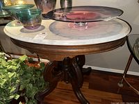 Full view of the round side table showing the white marble top with decorative glass bowls on it and the carved wooden base.