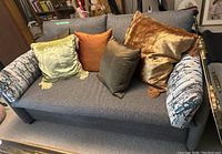 Front view of gray fabric hide-a-bed sofa with cushions and five throw pillows in assorted colors