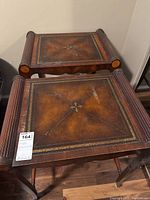 Two square wooden tables with decorative, worn tops and carved column legs