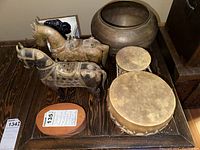 Two decorative wood and metal horses, large brass bowl and two ceramic drums arranged on wood surface