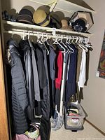 Photo of hangers with women's coats, jackets, and scarves on a closet rod along with bags in storage tubs below.
