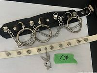 Photo showing two gothic style chokers; one black leather with large metal rings and chains, one white with metal spikes and a Playboy bunny charm.