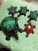 Five ceramic turtles of varying sizes and colors from Blue Mountain Pottery, arranged on a light green cloth.