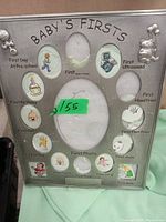 Front view of the silver-tone Baby's Firsts picture frame showing all photo cut-outs labeled with baby's milestones and baby-themed decorative motifs.