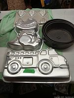 Photo showing novelty baking pans including a fire truck shape, dinosaur shape, six-cup muffin pan, and two black springform pans.