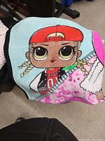 Child's blanket showing a large LOL Surprise doll character with braids and a red cap printed on it