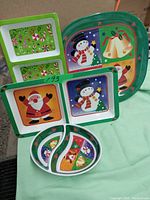Photo of five Christmas themed plastic trays showing different festive holiday designs and colors, including Santa, snowman, bells and peppermint candy images.