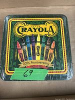 Front view of sealed square metal Crayola collector tin with vintage design and 90th anniversary text.
