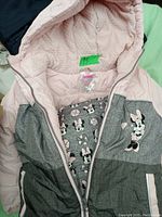 Front view of pink and grey Minnie Mouse coat, zipper open showing Minnie Mouse patterned lining and Minnie Mouse graphic on left chest.