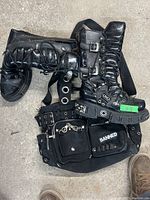 Top view showing the black Gof boots with buckles and metal accents, the Banned purse, and the black grommet belt laid out together.