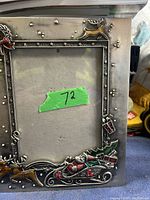 Front view of the metal picture frame showing the Christmas design in relief including Santa in a sleigh with presents, a reindeer, and snowflakes.