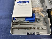Opened carrying case showing Kreg Jig Jr pocket hole jig, drill bits, wooden plugs, user manual and metal hardware pieces.