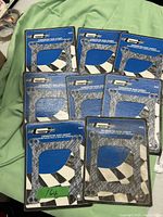 Lot of 8 sealed Holley 4bbl carburetor base gaskets in blue black packaging, arranged on light green fabric.