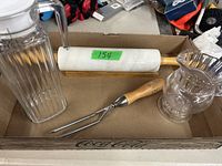 Photo showing a marble rolling pin with wooden handles, a tall ribbed glass pitcher, and a shorter clear decorative glass pitcher all placed in a cardboard box.