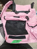 Image of a small pink pet carrier tote bag with black mesh ventilation and multiple pockets on a flat surface.