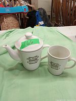 White ceramic Tim Hortons branded tea pot with lid and matching ceramic cup on a green cloth background.