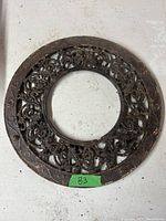 Round cast iron stove pipe grill showing decorative floral and scroll design with a hollow central opening. Rust and wear evident from age.