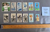 Top view of 12 vintage golf cards laid flat with ruler for size reference, showing portraits and action shots of golfers.