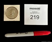 Front side of Eddie Shack coin in protective cardboard holder alongside Sharpie pen and lot number card for scale.