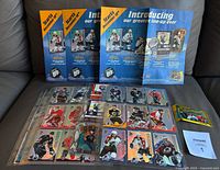 Complete set of hockey cards in clear binder pages with three McDonald's hockey card menus laid behind and an unopened wax pack to the right on a grey surface